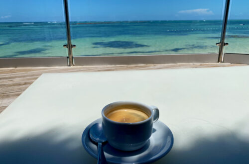 Coffee on a white table with ocean in the background. Nancy's summer blogging challenge