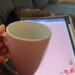 Hand holding pink coffee cup with iPad screen in background. Escape from routine prison