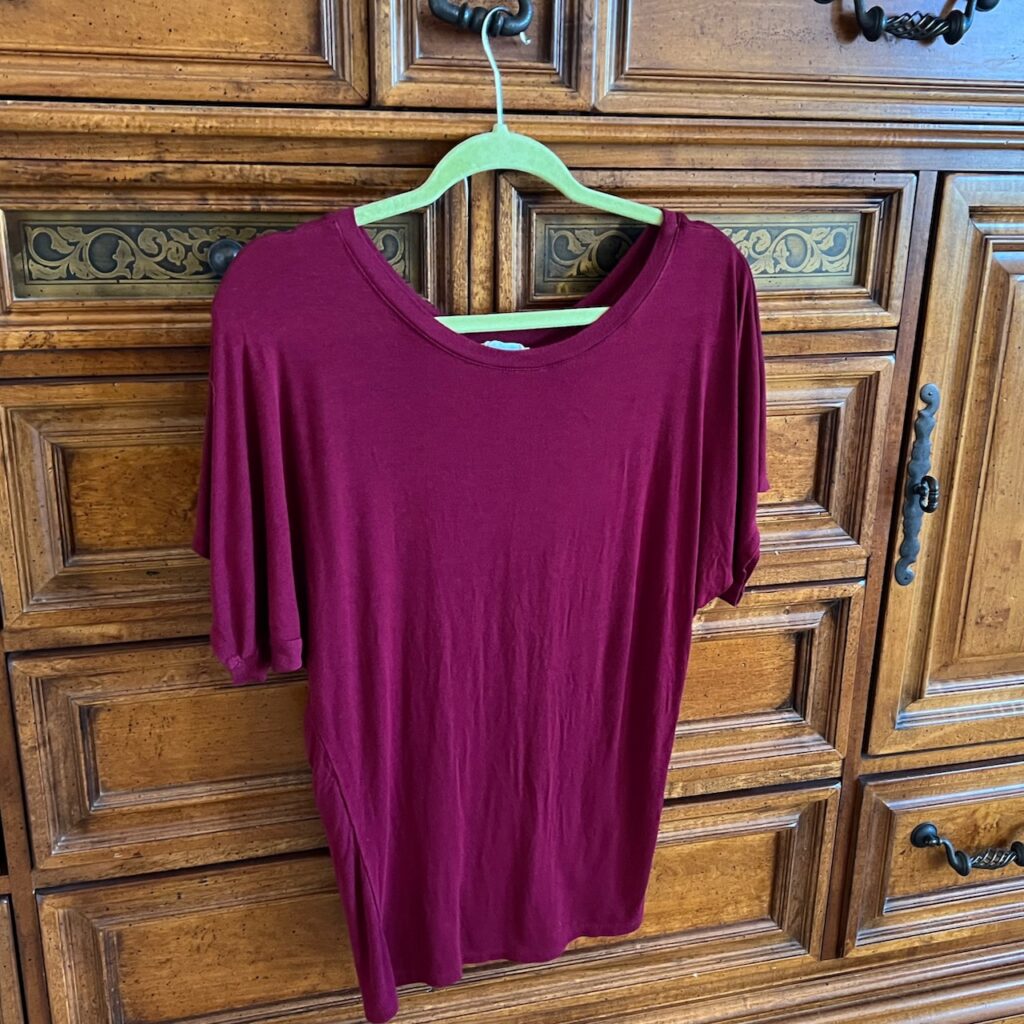 Burgundy dolman sleeved shirt hanging up in front of a dresser