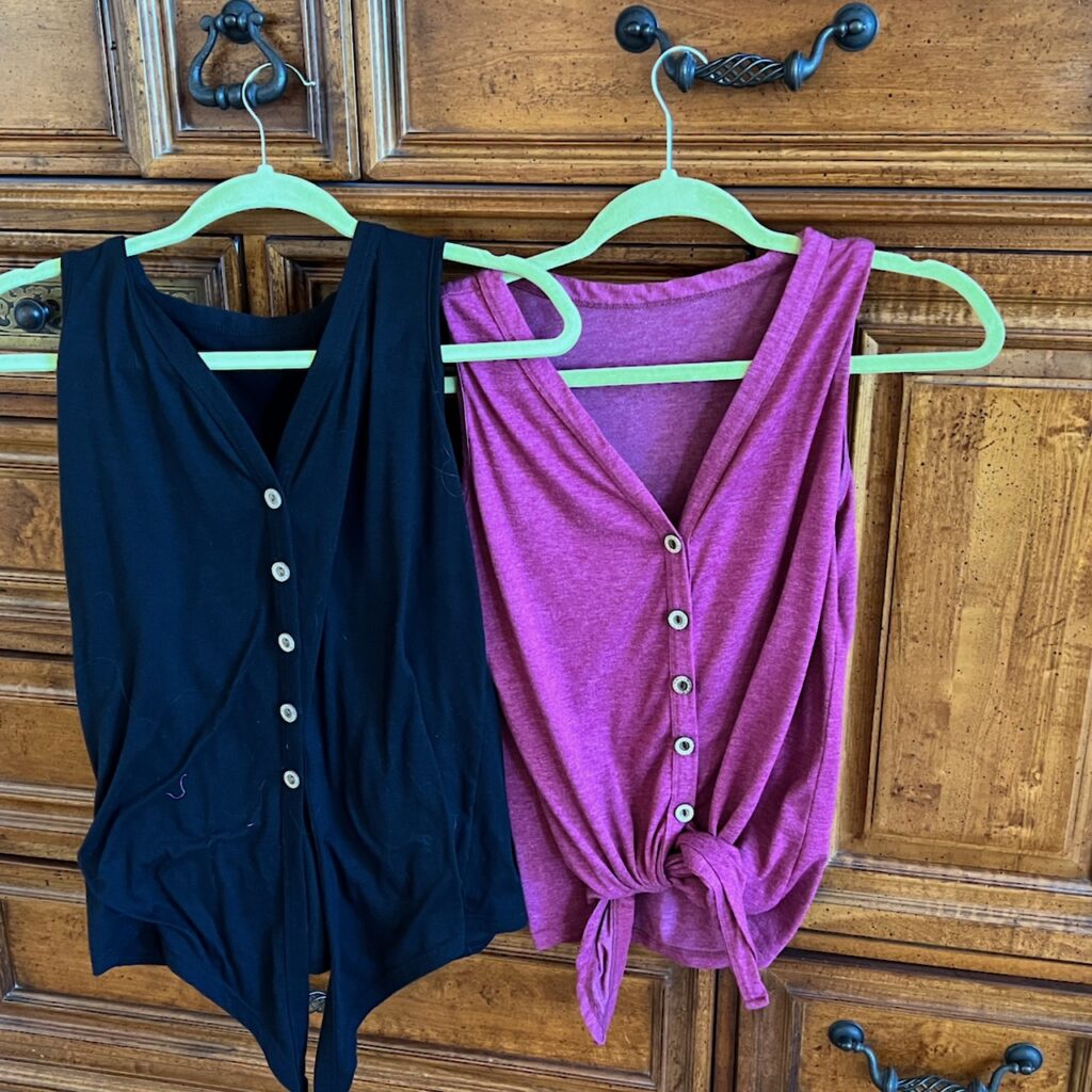 Two button front shirts hanging. One is black and the other is pink