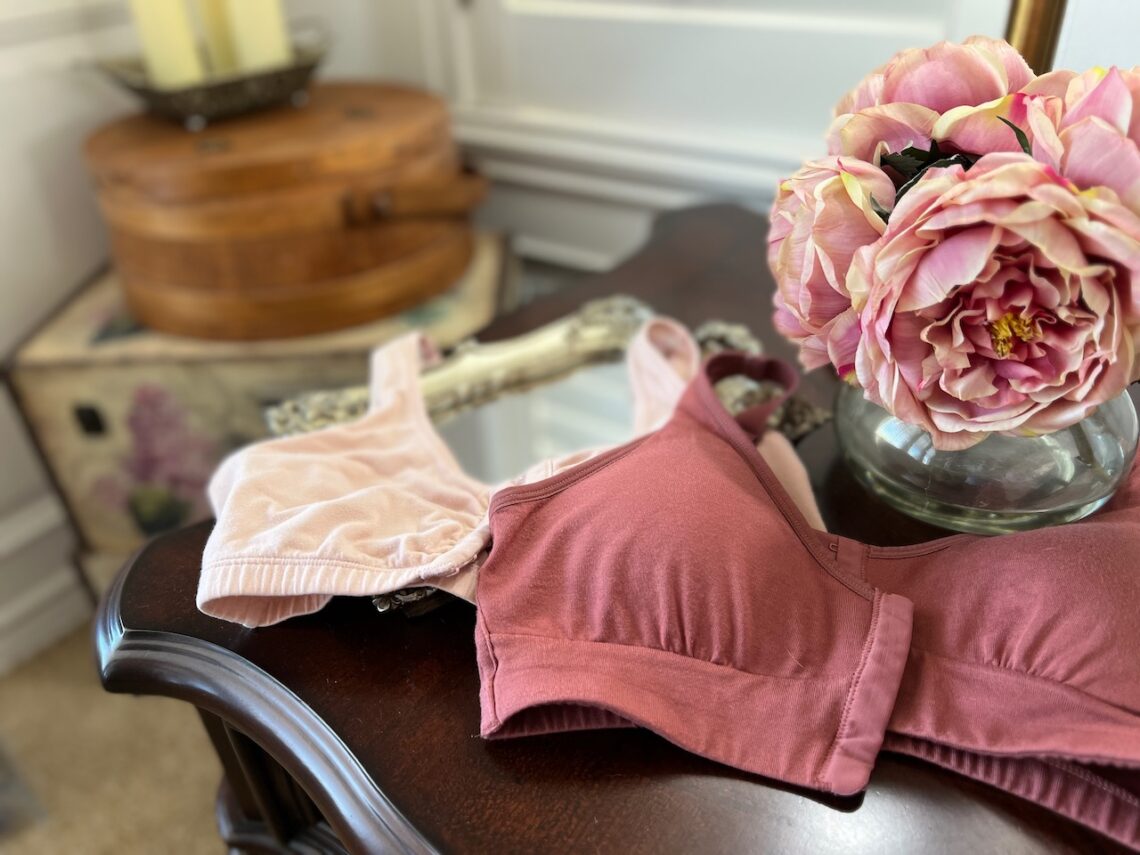 Two pink bras on an end table with pink roses in the background. My two favorite lumpectomy recovery bras.