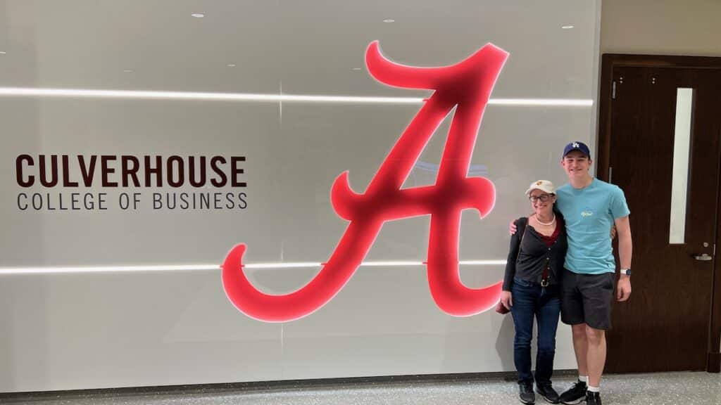 Author and son standing in front of Culverhouse business school sign with red Alabama A