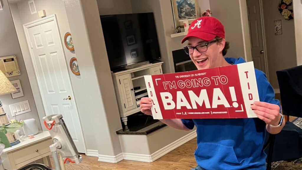 Author's Son holding a I'm going to Mama sign wearing an Alabama hat