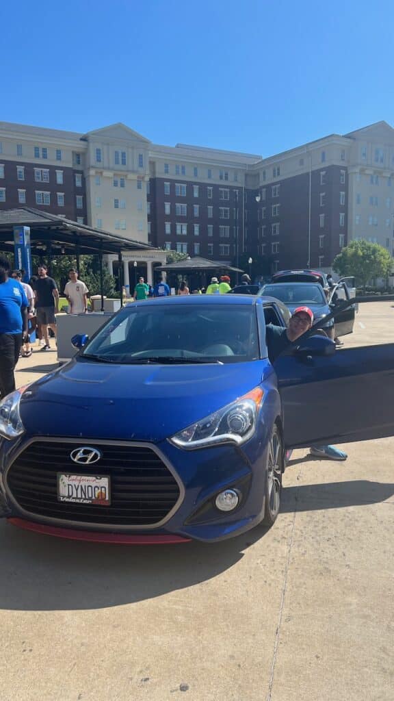 Blue Veloster with driver side door open and author's son stepping out. Parked in front of a university residence hall