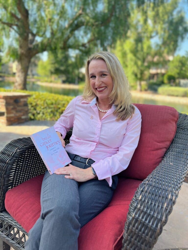 Author outside in a red chair holding a copy of "A Breast Cancer Journey:Living It One Step at a Time