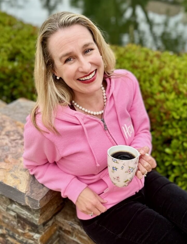 Author in a pink sweatshirt holding a cup of coffee