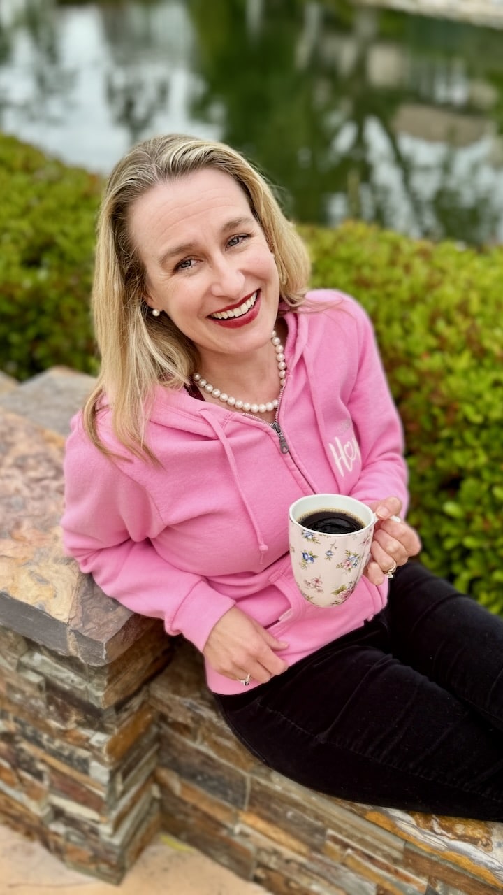 Author in a pink sweatshirt holding a cup of coffee