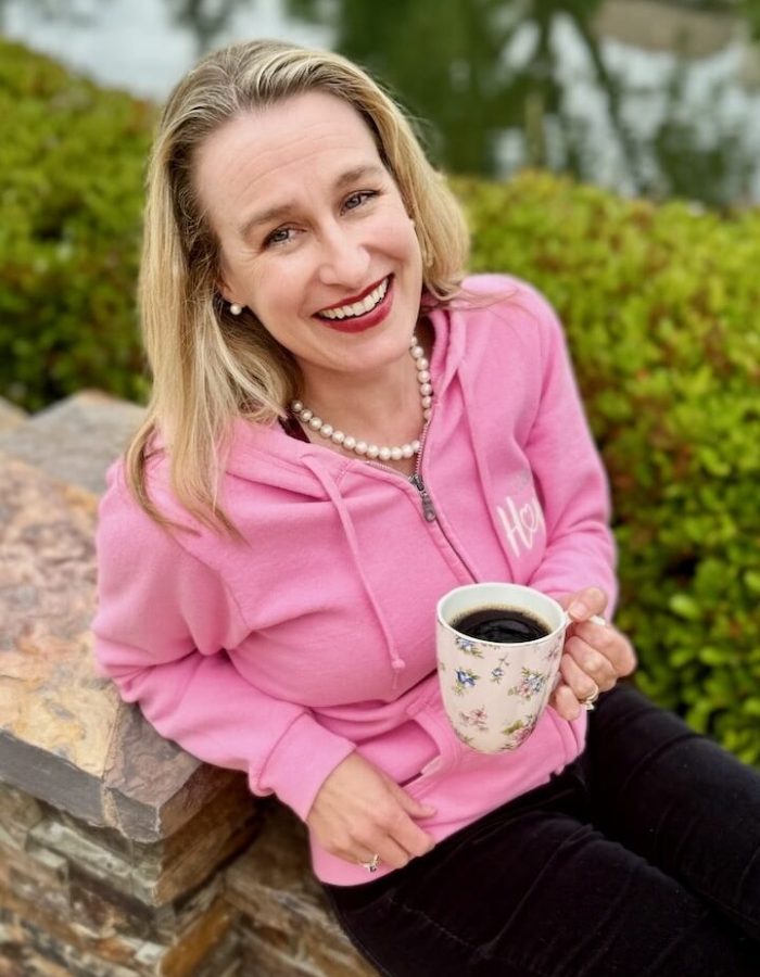 Author in a pink sweatshirt holding a cup of coffee