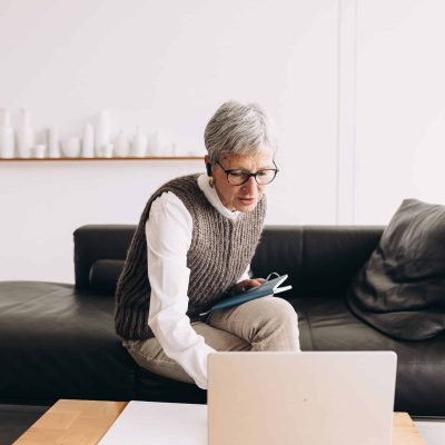 woman with gray hair sitting on a couch reaching for a laptop